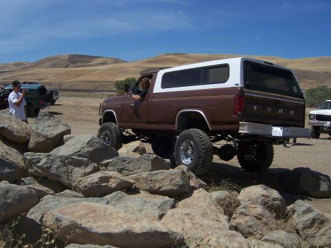 1991 Ford Bronco - Modified Ford pickup truck navigates rocky terrain with a white camper shell.