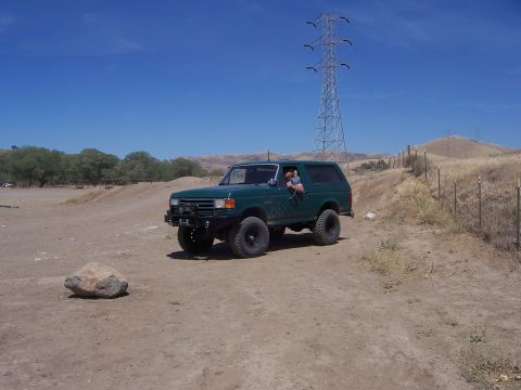 1991 Ford Bronco - A green 1991 Ford Bronco drives on a dirt road with a power line tower in the background.