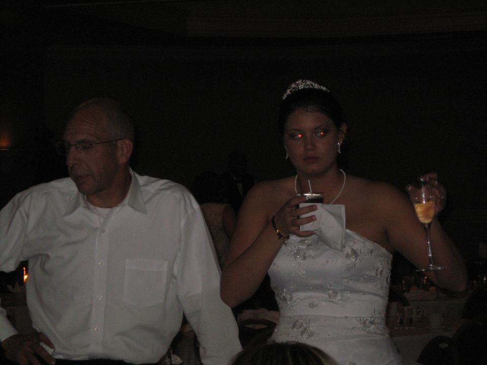Man in white shirt and woman in wedding dress holding drinks at an event