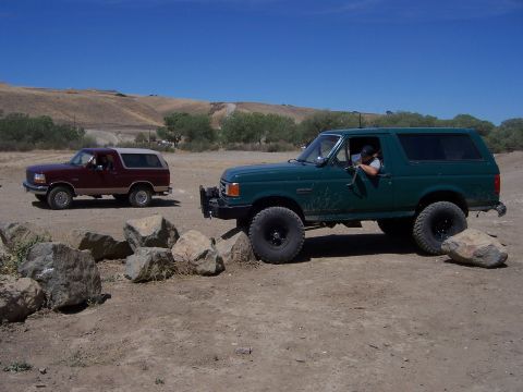 1991 Ford Bronco - Two Ford Broncos navigate a rocky, off-road trail under a clear blue sky.