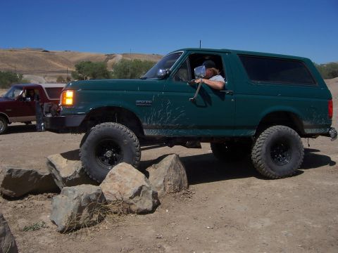 1991 Ford Bronco - A green 1991 Ford Bronco navigates an off-road obstacle course with another vehicle visible in the background.