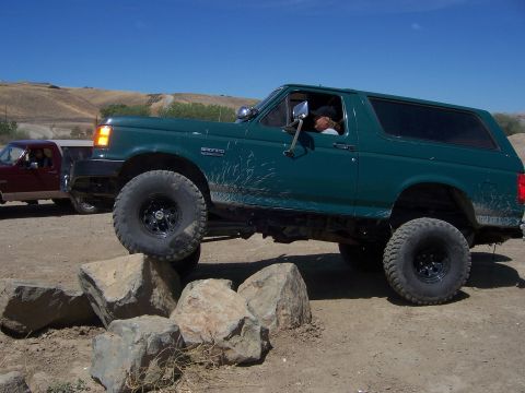 1991 Ford Bronco - A green 1991 Ford Bronco navigates an obstacle course of rocks under a clear blue sky.