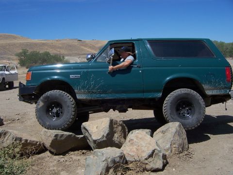 1991 Ford Bronco - A green 1991 Ford Bronco navigates a rocky obstacle course on a sunny day.