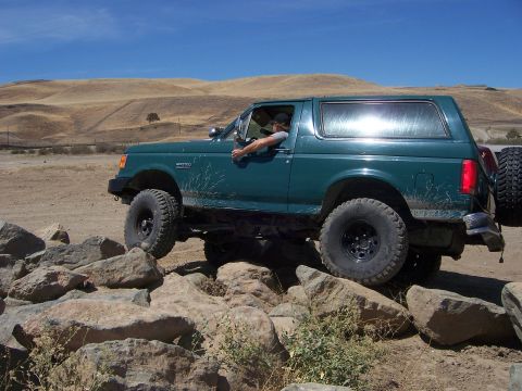 1991 Ford Bronco - A green Ford Bronco navigates a rocky terrain on a sunny day.
