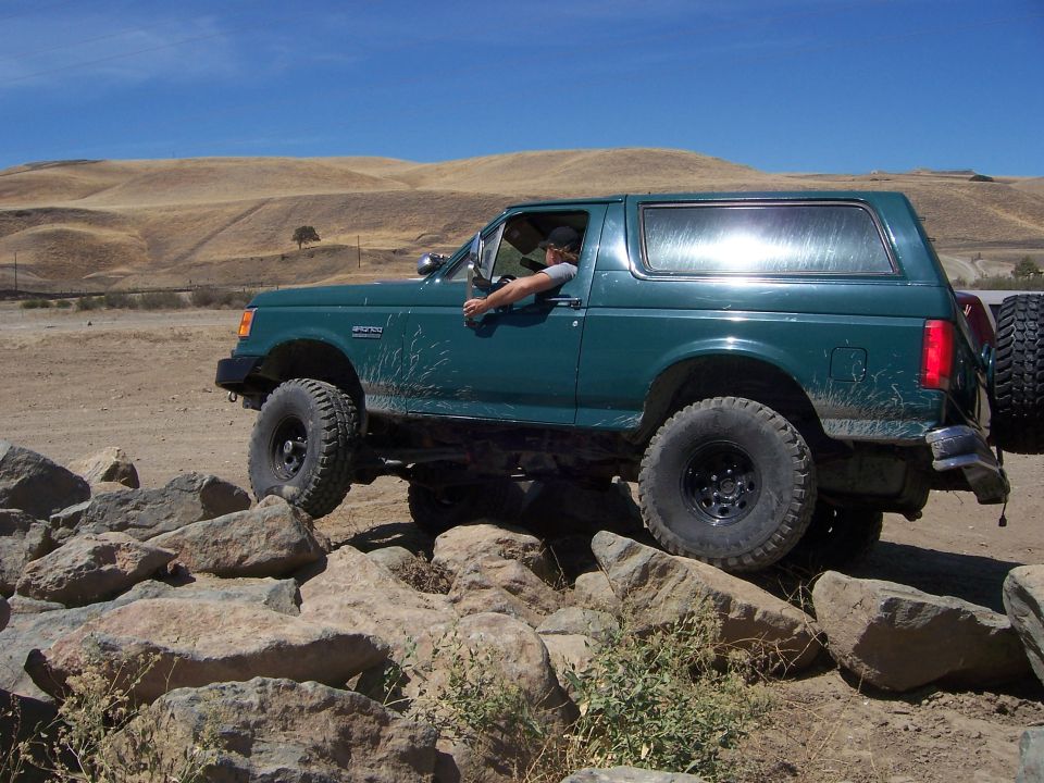 Green Ford Bronco with off-road tires climbing over rocks