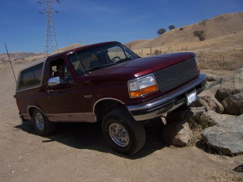 1991 Ford Bronco - Maroon Ford Bronco navigating rocky terrain under a clear blue sky.