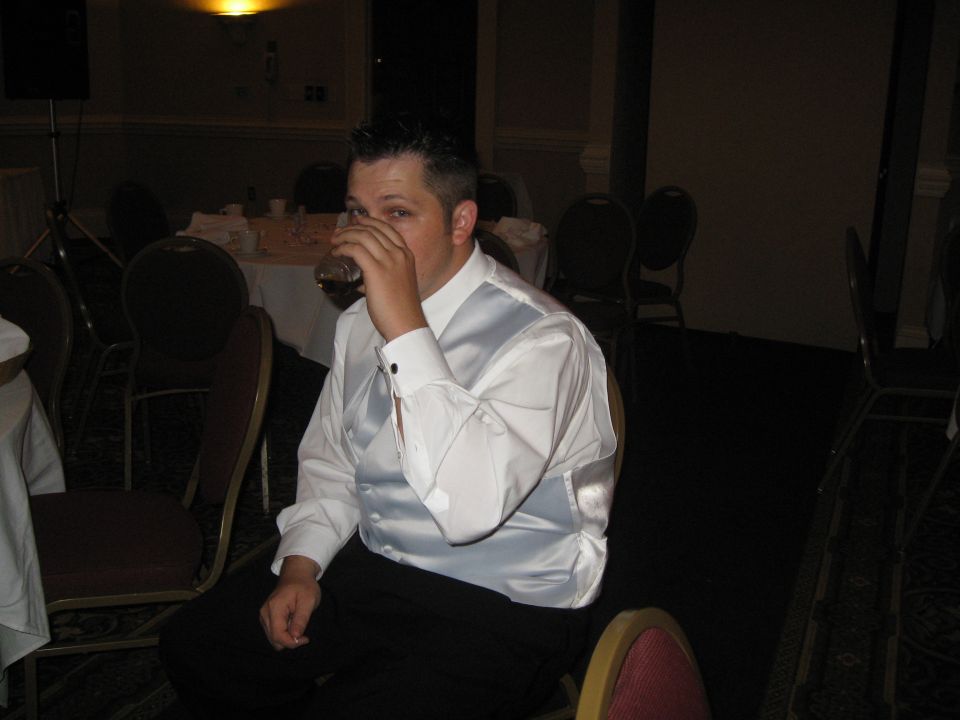guy in a vest and shirt drinks from a glass at a reception