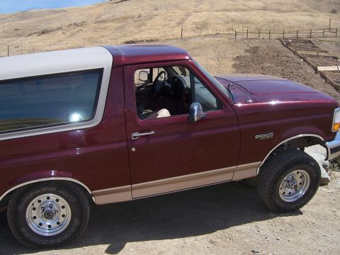 1991 Ford Bronco - Maroon and tan 1991 Ford Bronco parked on a dirt road with a hillside in the background.