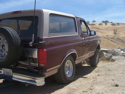1991 Ford Bronco - Maroon 1991 Ford Bronco with a tan top parked off-road on a sunny day.