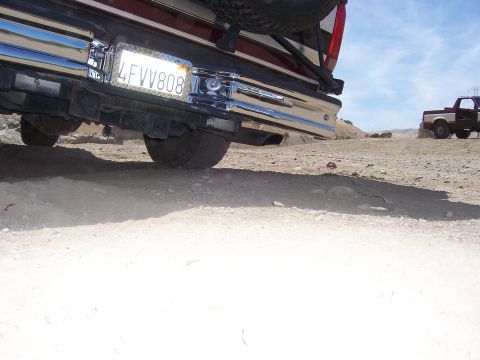 1991 Ford Bronco - The rear of a 1991 Ford Bronco is shown on a dusty, off-road terrain with another vehicle visible in the background.