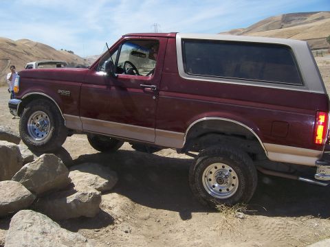 1991 Ford Bronco - A maroon 1991 Ford Bronco with a tan top navigates a rocky trail on a sunny day.