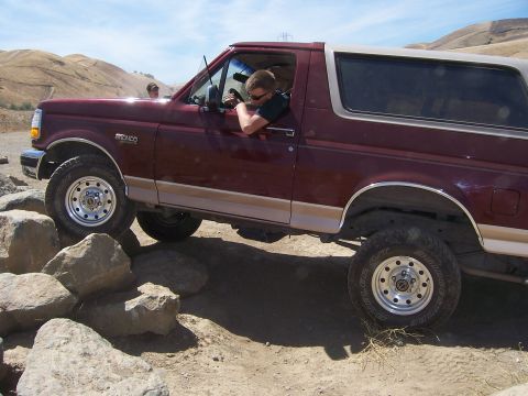 1991 Ford Bronco - A driver navigates a rocky trail in a maroon Ford Bronco with a tan removable top.