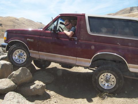 1991 Ford Bronco - A maroon Ford Bronco navigates a rocky trail on a sunny day.