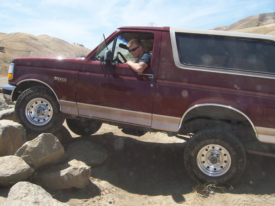 Maroon Ford Bronco driving over rocks, driver visible