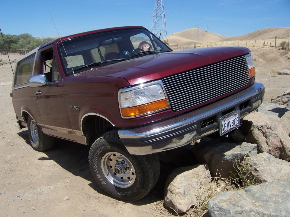 Maroon Ford Bronco driving over rocks on a dirt path. License plate reads 4FVV808