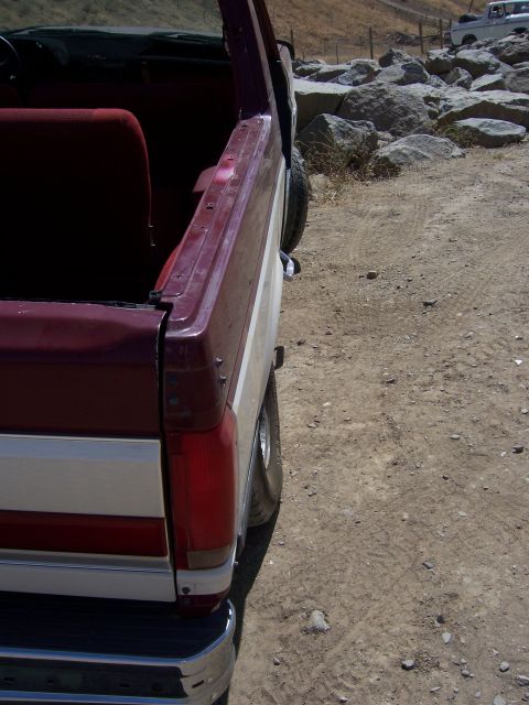 1991 Ford Bronco - A maroon and white Ford Bronco is parked on a dirt road, with another vehicle visible in the background.