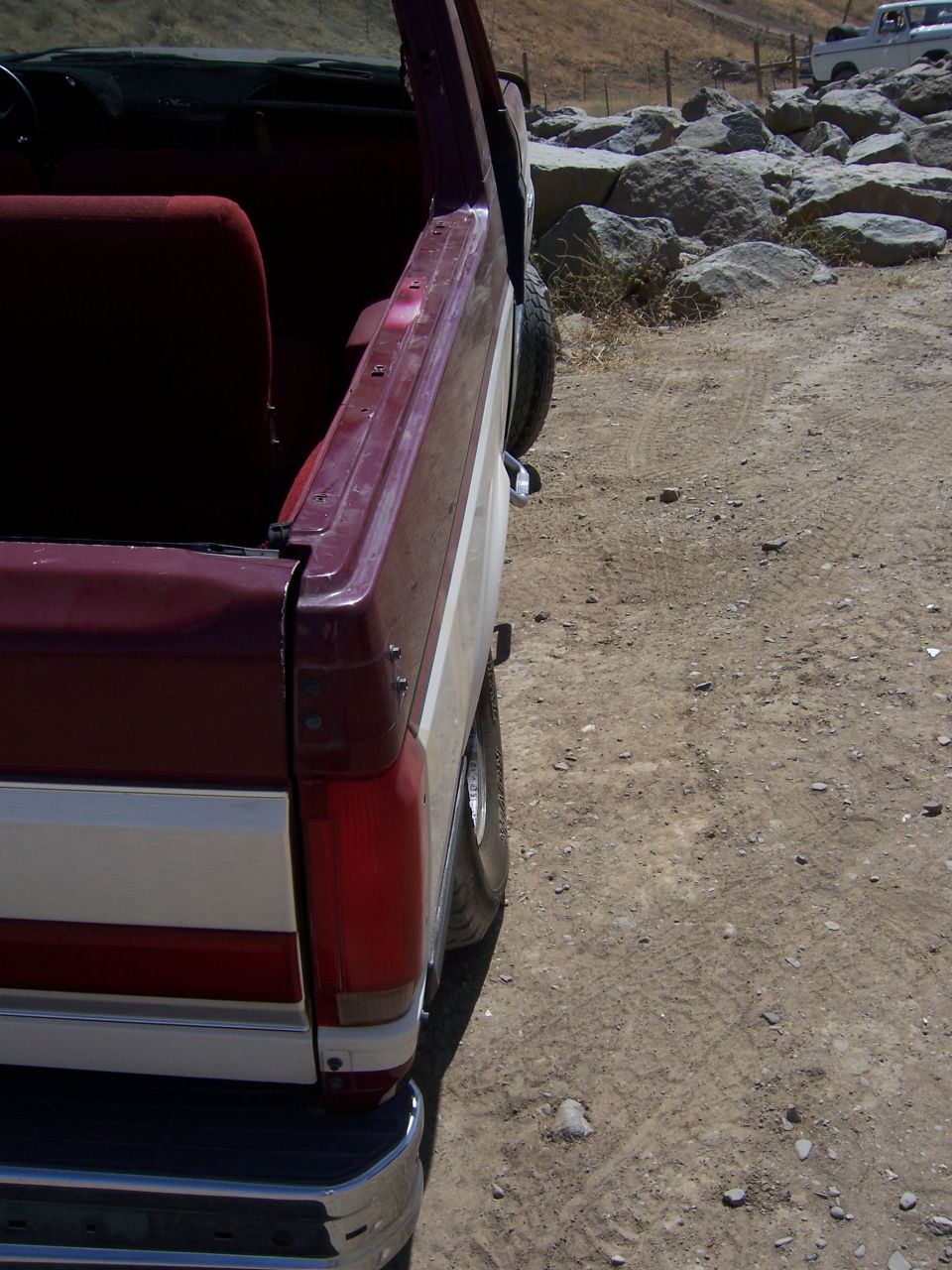 Maroon and white Ford Bronco rear quarter panel, showing a portion of the interior and a tire. Another white vehicle is visible in the background