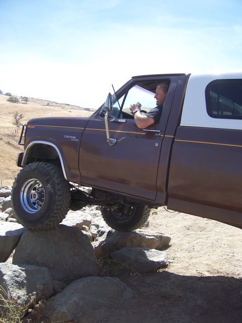 1991 Ford Bronco - A brown 1991 Ford Bronco Custom F-250 with a white camper shell navigates a rocky trail.