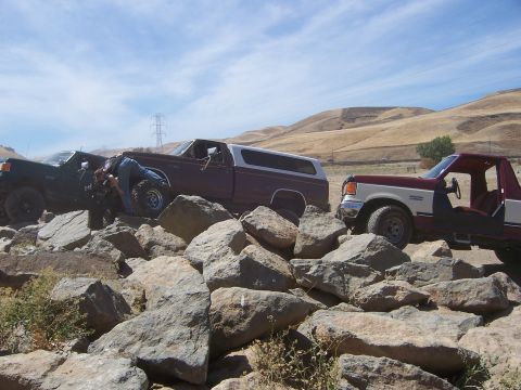 1991 Ford Bronco - Three Ford Broncos traverse a challenging rocky landscape under a bright blue sky.