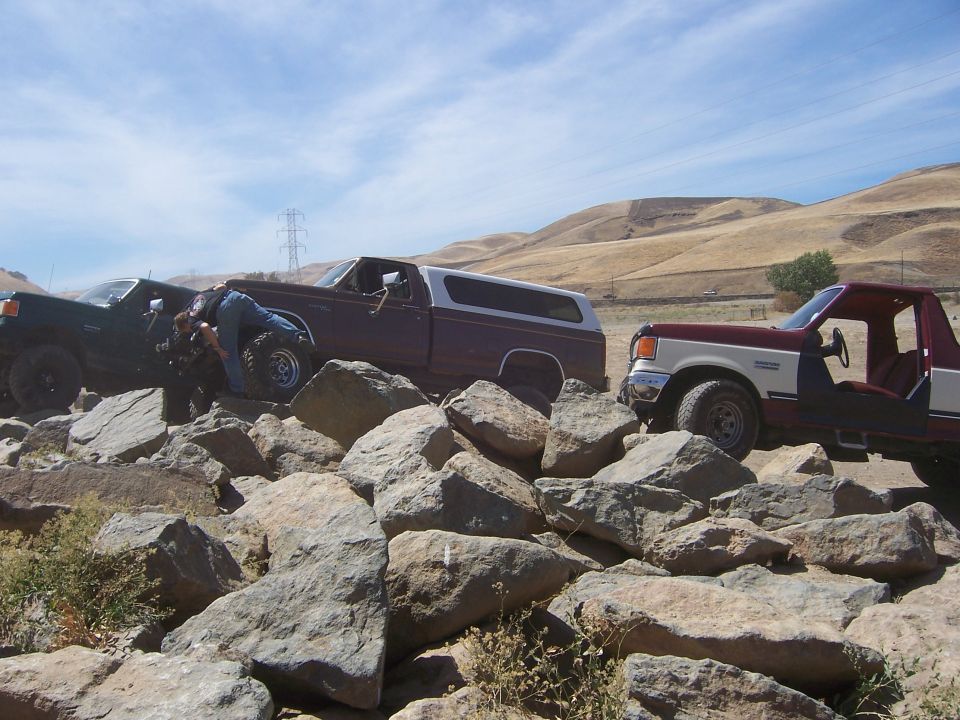Maroon and white Ford Bronco with a white camper shell navigating rocky terrain