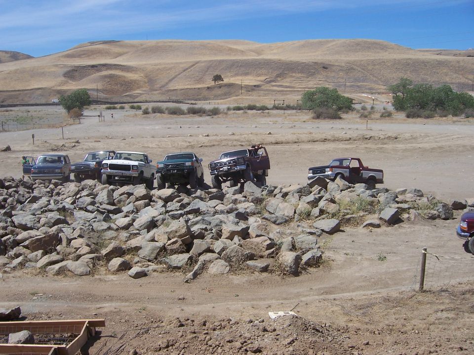 Several trucks and SUVs are parked on a rocky incline in a dry, hilly landscape