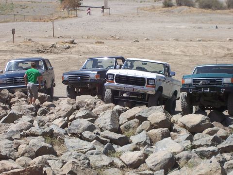 1991 Ford Bronco - Several off-road vehicles, including a white pickup truck, traverse a rocky landscape on a sunny day.
