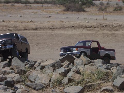 1991 Ford Bronco - Two trucks navigate a rocky terrain under a dry, dusty sky.