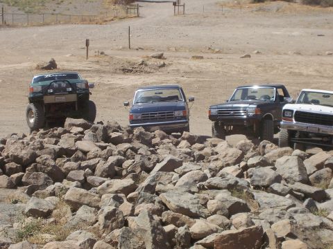 1991 Ford Bronco - Multiple Ford trucks and SUVs are parked on a rocky surface, with one green Bronco prominently lifted.
