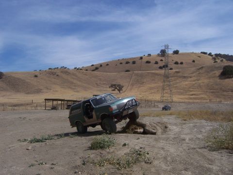 1991 Ford Bronco - A modified green SUV navigates an off-road obstacle course with a second vehicle visible in the distance.