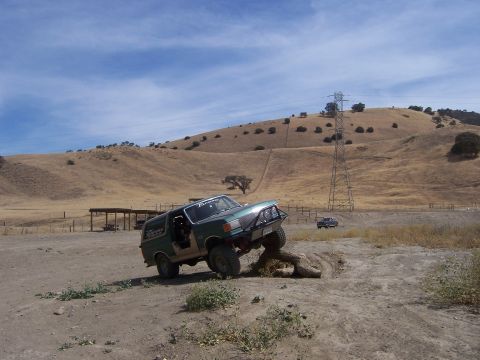 1991 Ford Bronco - A green 1991 Ford Bronco navigates an obstacle on a dry, hilly terrain under a blue sky.
