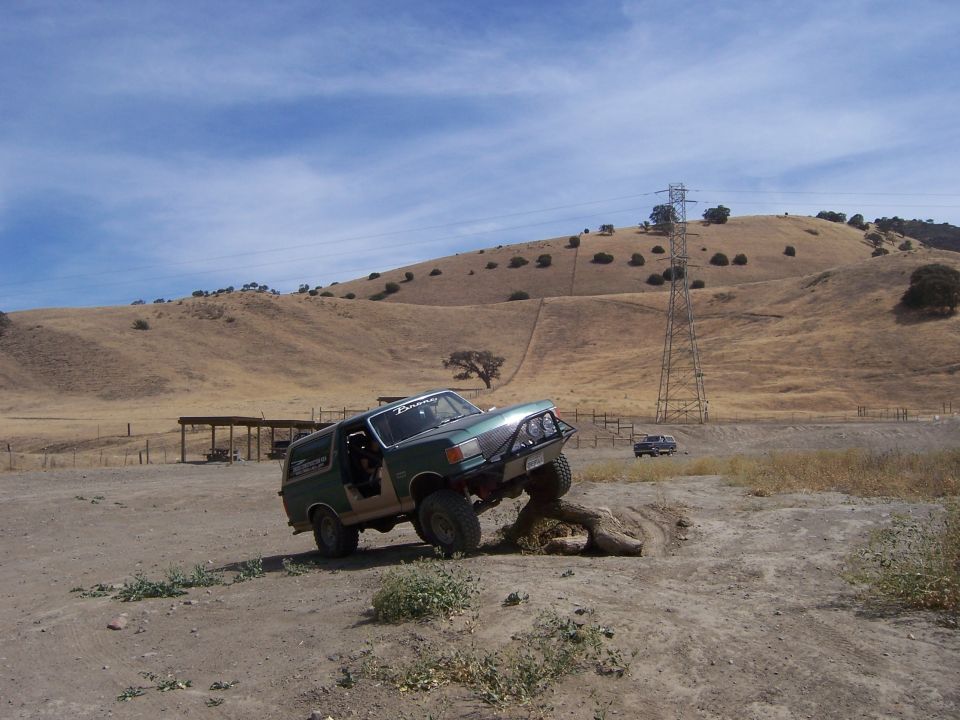 Green 1991 Ford Bronco climbing over a log on a dirt trail