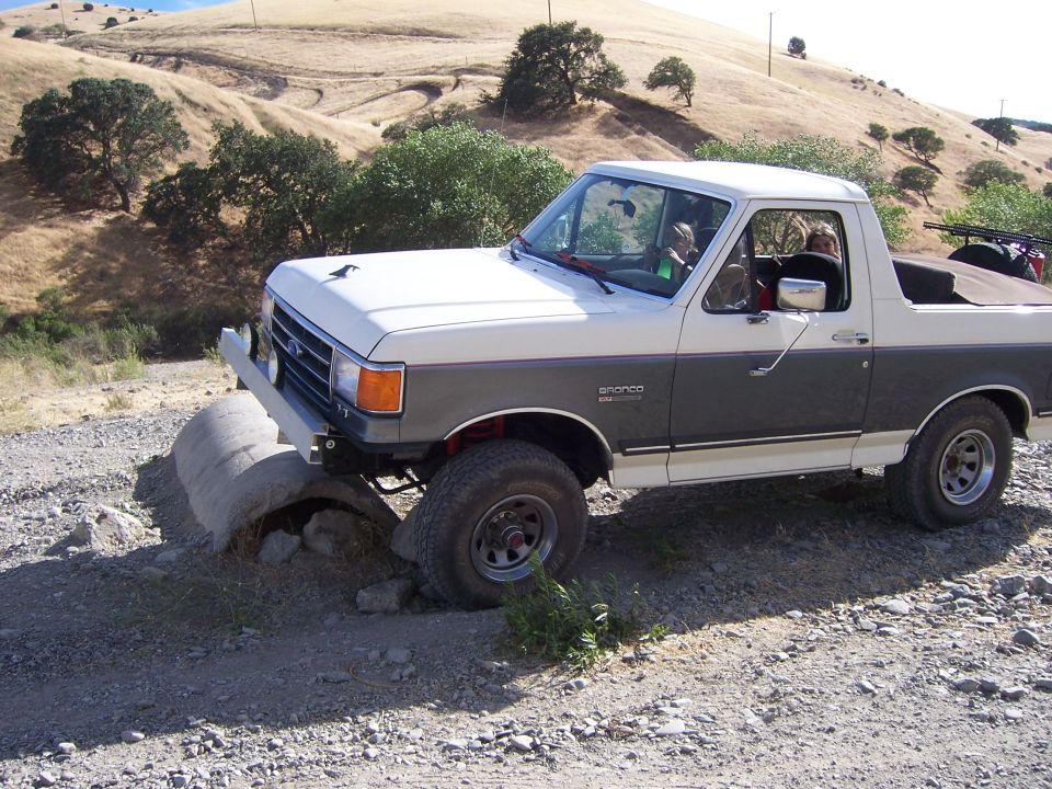 1991 Ford Bronco driving over concrete pipes on a dirt road