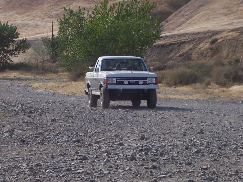 1991 Ford Bronco - A white Ford F-150 pickup truck navigates a rocky, off-road path under a clear sky.