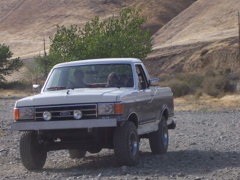 1991 Ford Bronco - A two-tone Ford F-Series truck with 4x4 badging is seen from the front-right on a gravel road.