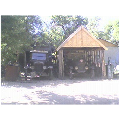 1973 Ford Ranchero - Two old trucks are parked outside, one partially sheltered by a wooden structure.