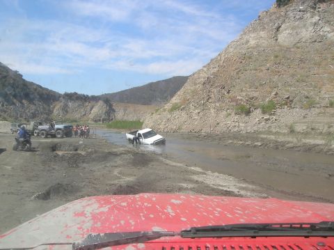 1985 Ford Bronco - Several vehicles and people are gathered around a white pickup truck stuck in a muddy, watery area.