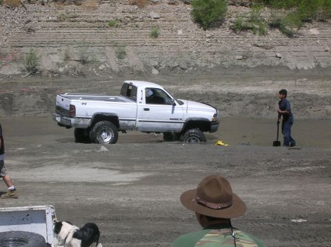 1985 Ford Bronco - A white pickup truck is stuck in the mud, with a person nearby holding a shovel.