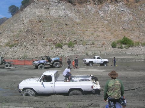 1985 Ford Bronco - Off-road vehicles are stuck in a muddy area with people observing and trying to help.