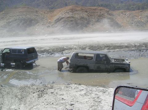 1985 Ford Bronco - Two SUVs are stuck in a muddy area, with one vehicle attempting to pull the other out.