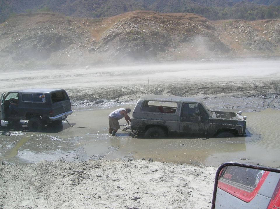 Two SUVs stuck in mud, one being pulled by the other. The front SUV has its hood open