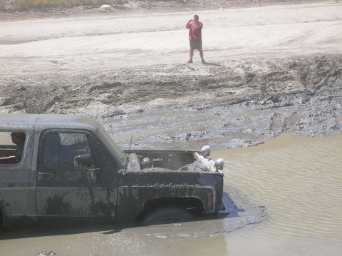 1985 Ford Bronco - Off-road vehicle submerged in mud and water, with its hood open.