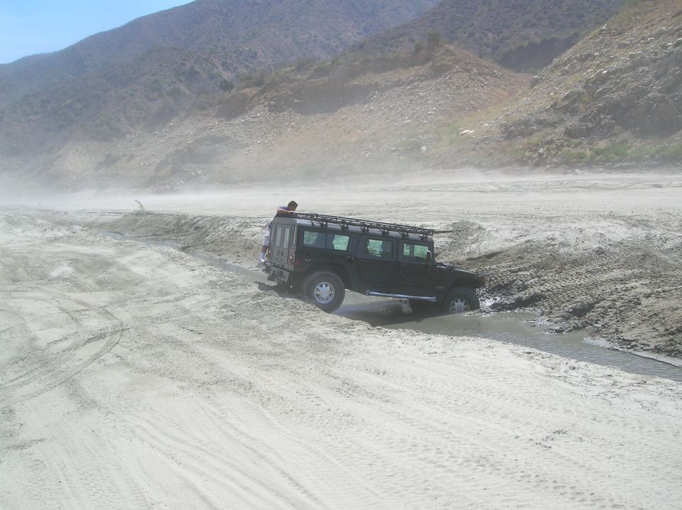 Black SUV with roof rack driving through water and sand in a desert landscape