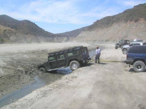 1985 Ford Bronco - A Hummer is stuck in a muddy ditch while other vehicles wait nearby to assist.