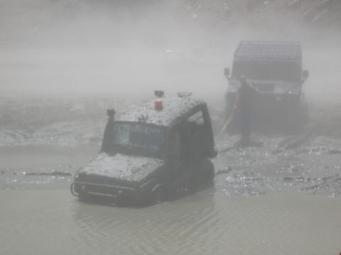 1985 Ford Bronco - Off-road vehicles are stuck in a muddy area, with one vehicle partially submerged in water.
