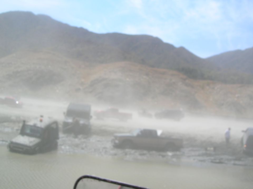 Several off-road vehicles navigate a muddy, dusty landscape with hills in the background