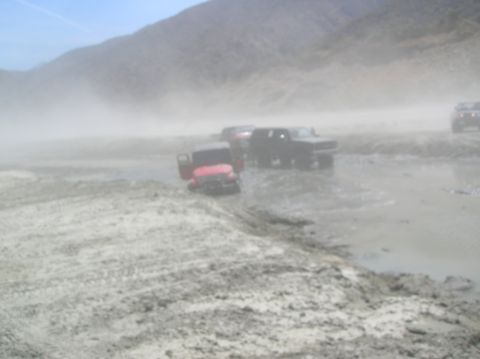 1985 Ford Bronco - Off-road vehicles navigate a muddy terrain, kicking up dust.