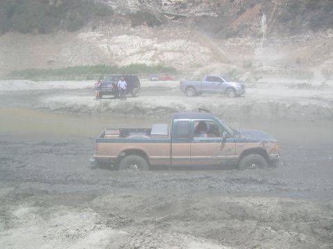 1985 Ford Bronco - Several vehicles are in a muddy area, with one pickup truck deeply stuck in the mire.