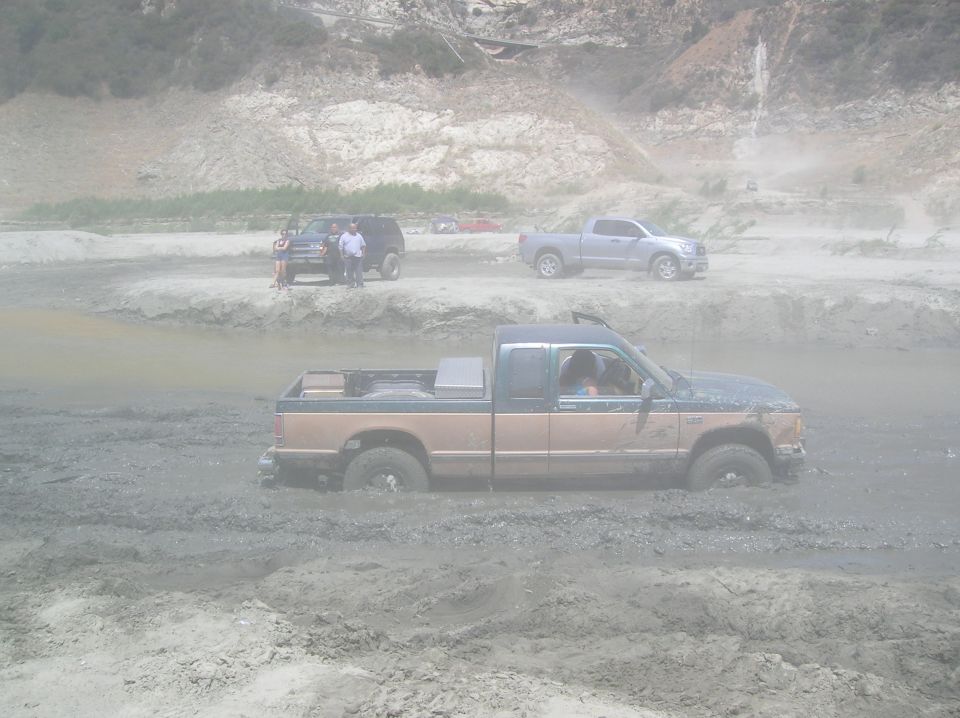 Pickup truck stuck in mud pit with other vehicles nearby