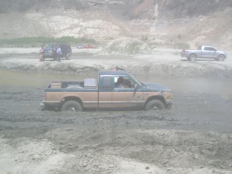 1985 Ford Bronco - Multiple vehicles navigate a muddy off-road course.