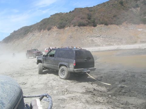 1985 Ford Bronco - Several off-road vehicles navigate a muddy terrain, with one SUV being towed.